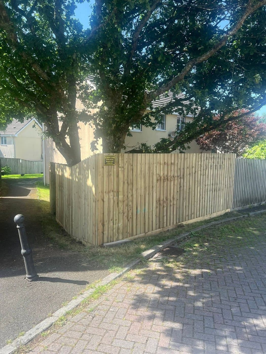 A close-board fence with a Gilbert & Son sign on it, alongside a footpath